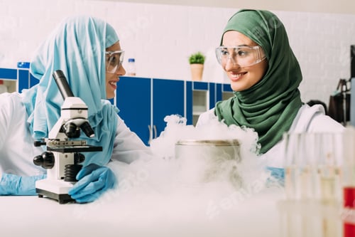 Preview: smiling female muslim scientists experimenting with microscope and dry ice in chemical laboratory