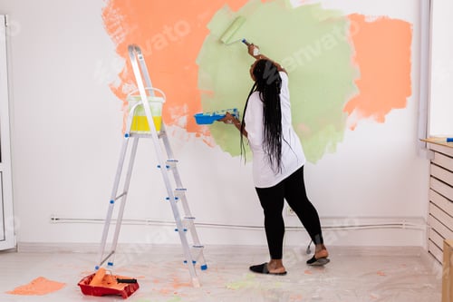 Preview: Beautiful african american girl painting the wall with paint roller.