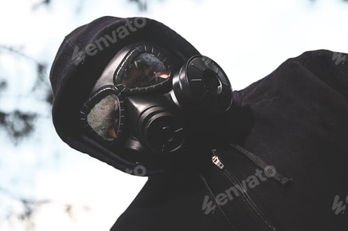 Preview: Low angle shot of a person wearing a gas mask and black jacket in the ranch during a quarantine