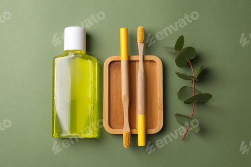 Preview: Fresh mouthwash in bottle, toothbrushes and eucalyptus branch on green background, flat lay