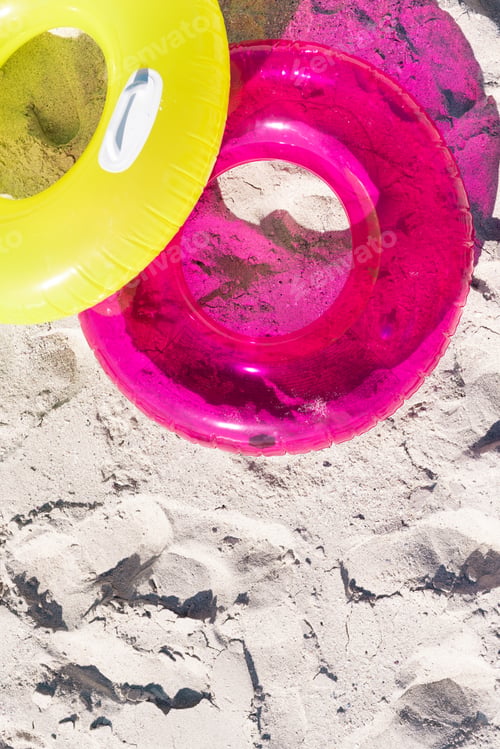 Preview: High angle view of pink and yellow inflatable swim rings on sandy beach during sunny day