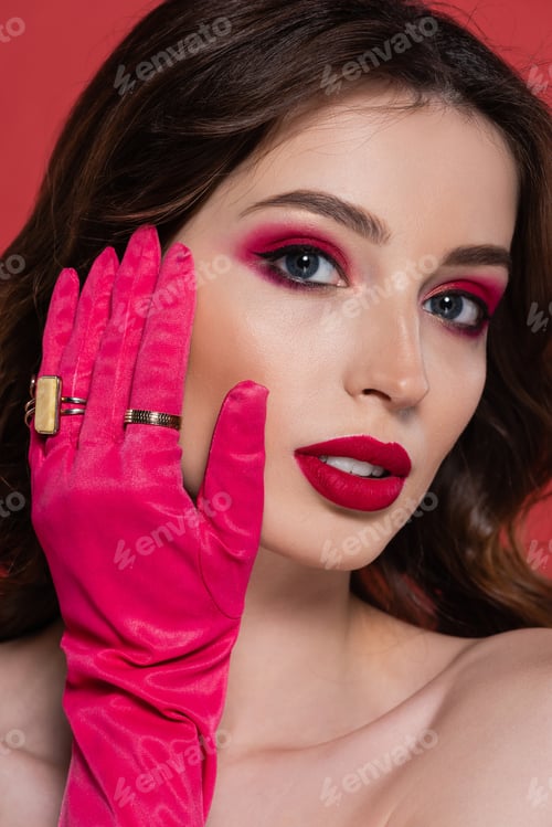 Preview: portrait of young woman with magenta color makeup and glove with golden rings isolated on pink