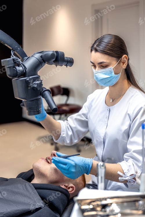 Preview: Young female dentist treating patient's teeth with dental microscope. Dentistry concept.