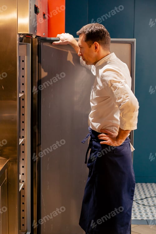 Preview: professional kitchen chef looks into the fridge and chooses ingredients for cooking food concept