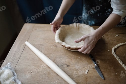 Vorschau: Eine Frau arbeitet und glättet den Rand eines Gebäckkastens, der eine Kuchenform auskleidet.