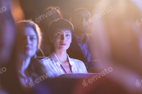 Preview: Front view of beautiful Asian businesswoman sitting in the auditorium and looking at camera