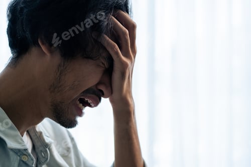Preview: Asian young upset depressed man sitting alone in living room at home.