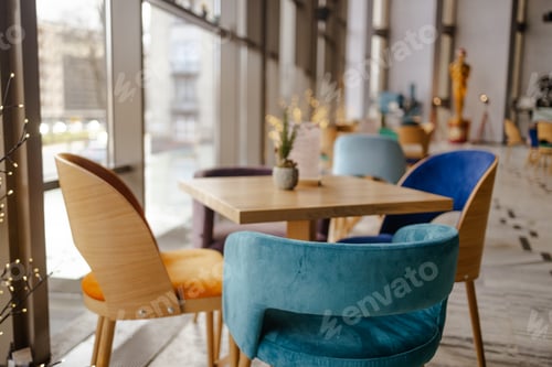 Preview: Modern white cafe interior with color tables with chairs standing next to them. Large windows and an