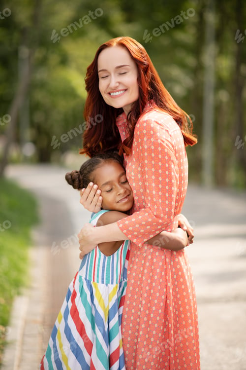 Preview: Beautiful red-haired woman smiling while hugging daughter