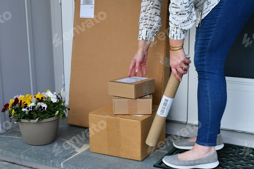 Preview: Woman picking up packages ordered online boxes off the front porch after they were delivered