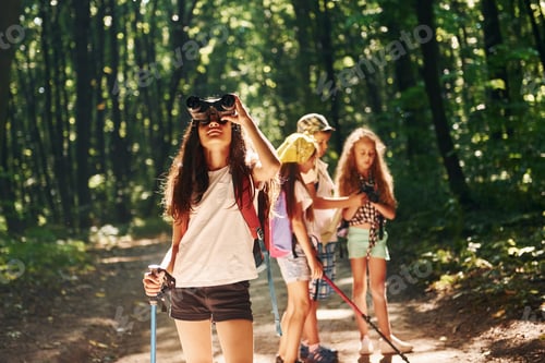 Preview: Girl standing in front of her friends. Kids strolling in the forest with travel equipment