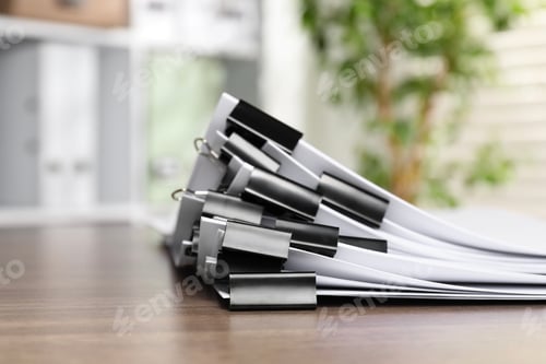Preview: Binder clips with sheets of paper on wooden table indoors, closeup