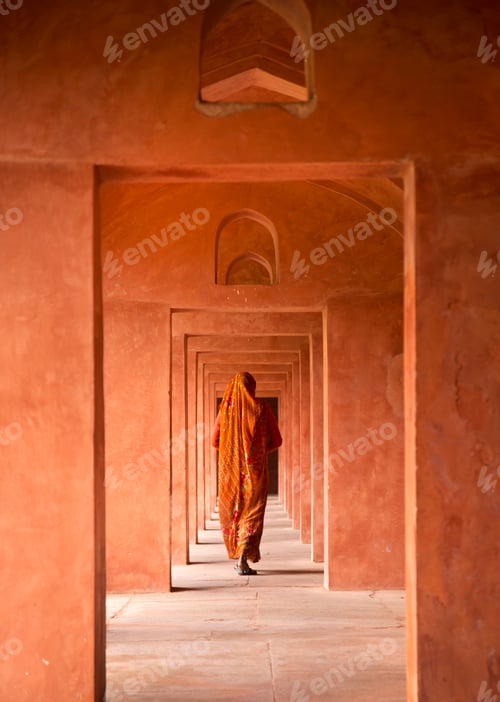 Preview: Rear view of woman wearing orange sari walking along passageway.