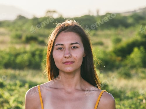 Preview: Portrait of young brunette woman posing in summer field in yellow dress. Mountain background view.