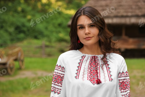 Preview: Beautiful woman wearing embroidered shirt in village, space for text. Ukrainian national clothes