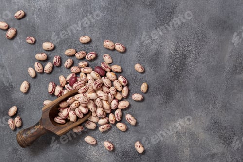 Preview: Wooden scoop full of dried pinto beans on gray top view. Traditional Latin American legumes