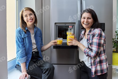 Preview: Two middle-aged women friends drinking orange juice in the kitchen