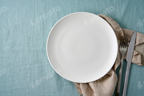 Preview: Placeit. Clean empty white plate, fork and knife on pastel blue aquamarine linen tablecloth on table
