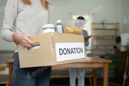 Vista previa: Beautiful female volunteer holds a donation box with canned food in it.