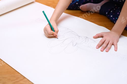Preview: kids hobby. little six year old child girl draws with a pencil on paper sitting on the floor at home