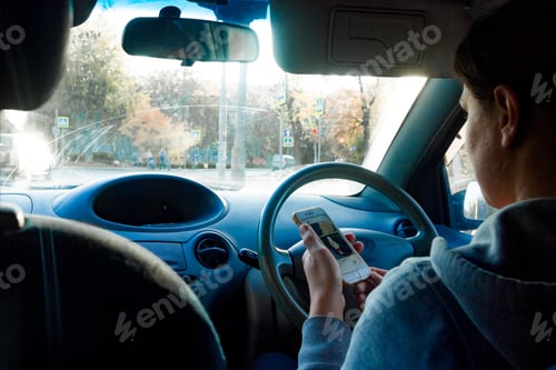 Preview: a young woman sits behind the wheel and looks at the phone in her hand
