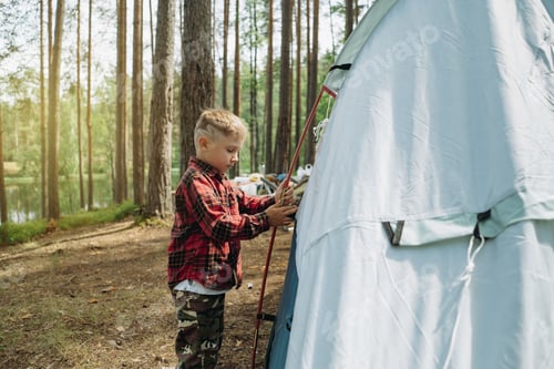 Preview: cute little caucasian boy putting up a tent. Family camping concept