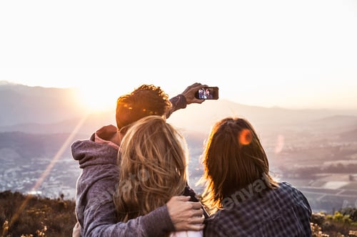 Preview: Rear view of friends on hillside taking selfie