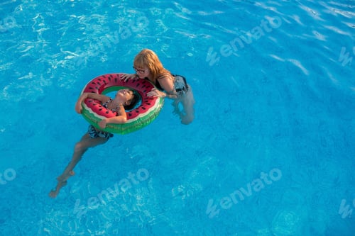 Preview: Mother and daughter holding onto inflatable ring in swimming pool