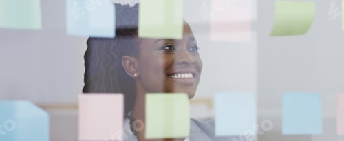 Preview: Businesswoman brainstorming with colorful sticky notes on glass wall