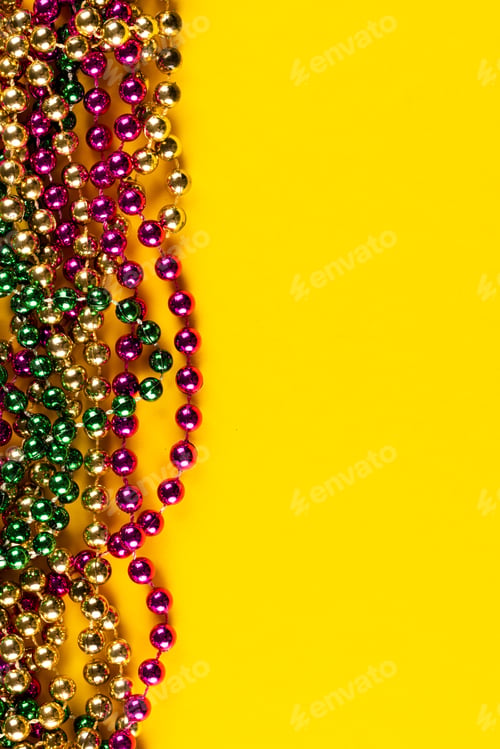Preview: Composition of colourful mardi gras beads on yellow background with copy space