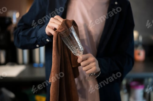 Preview: A bartender is meticulously polishing a wine glass with a brown cloth, ensuring it is spotless for t