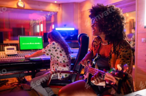 Preview: Diverse female bass player at recording studio playing guitar.