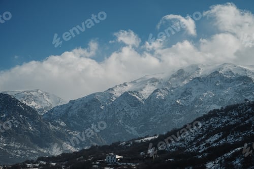 Preview: Panoramic view of snow-capped mountains against a blue cloudy sky.