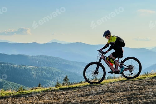 Vista previa: Hombre ciclista montando bicicleta de montaña eléctrica al aire libre por un sendero cubierto de hierba en las montañas.