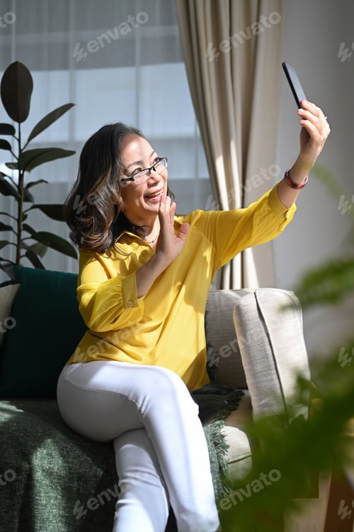 Preview: Smiling middle aged lady in casual clothes making with smart phone.