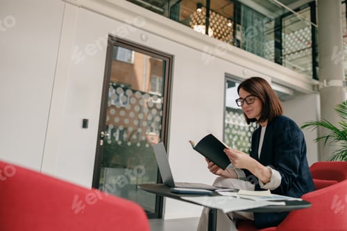 Preview: In a contemporary office, a female professional is focused on her work using a laptop and notebook