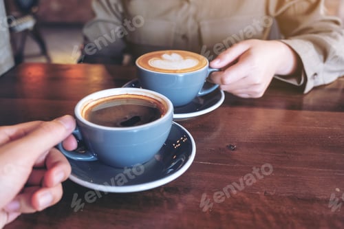 Preview: Close up image of a man and a woman clinking blue coffee mugs on wooden table in cafe