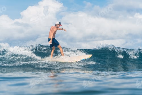 Preview: man in swimming shorts and cap surfing in ocean