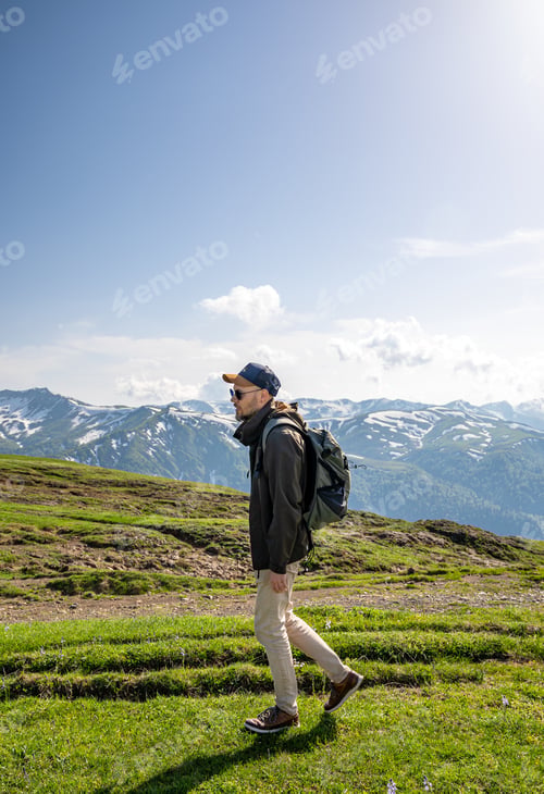 Preview: A tourist walks along a green mountain trail at summer day.