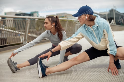 Preview: Beautiful sportive women doing stretching exercise on footbridge in the city