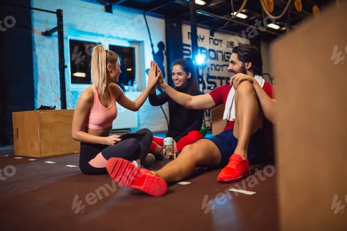Preview: Happy young athletic people in sportswear giving high five after workout in gym.