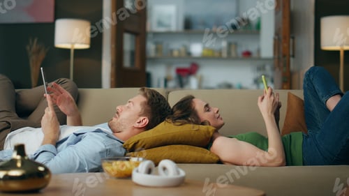 Preview: Relaxed pair browsing gadgets sofa. Woman texting telephone guy reading tablet