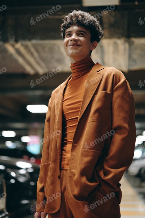Preview: Stylish young man in an orange outfit standing in a parking garage