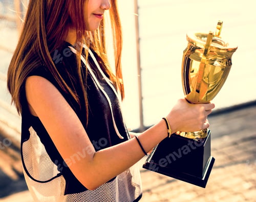 Preview: Asian teenage girl in sporty clothes holding a trophy outdoors