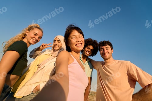 Preview: Happy multi ethnic friends taking selfie outdoors against blue sky