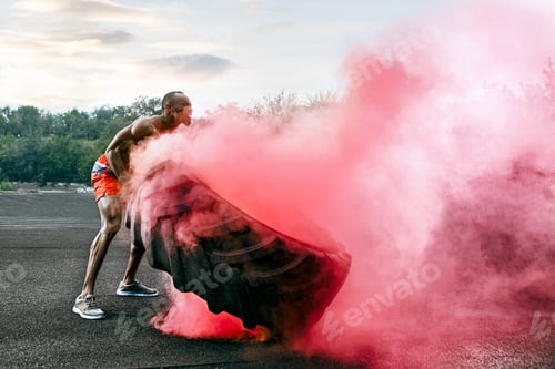 Preview: Handsome muscular man flipping big tire outdoor.