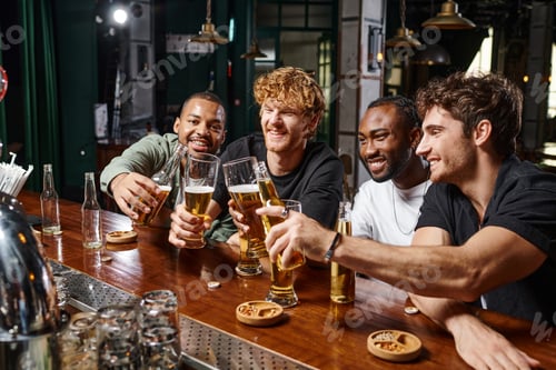 Preview: group of four happy multiethnic male friends toasting with glasses of beer at bar counter
