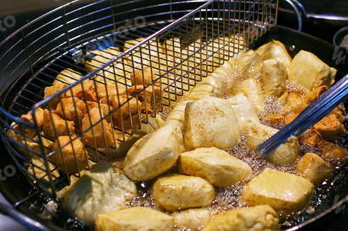 Preview: Close-up of golden brown stinky tofu frying in hot oil in a deep fryer.