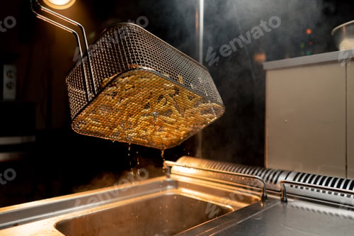 Preview: kitchen in the hotel restaurant the chef takes out delicious french fries from the fryer oil drips