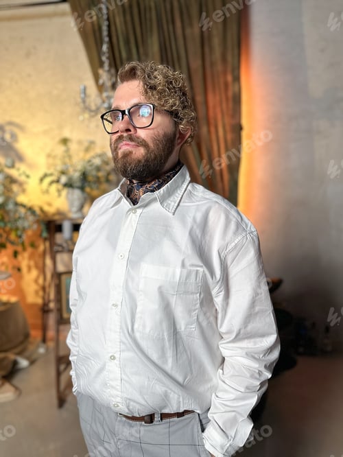 Preview: Thoughtful man in a white shirt stands confidently in a warmly lit room with a classic and elegant